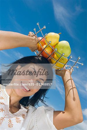 Vue d'angle faible d'une femme adulte mid tenant un plateau de fruits sur la tête et sourire