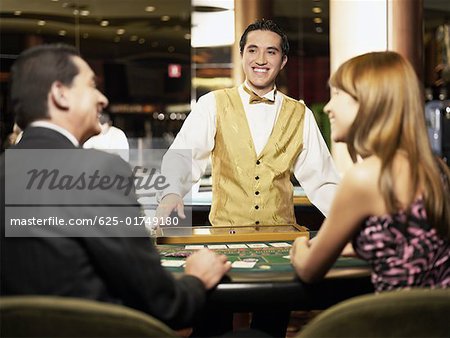 Vue arrière d'un homme d'âge mûr et une jeune femme assise à une table de jeu avec un travailleur de casino souriant devant eux