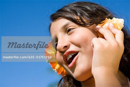 Close-up of a girl wearing flowers and listening to a conch shell