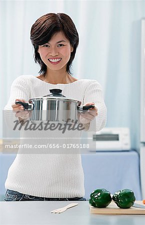 Woman in kitchen, holding crocking pot towards camera