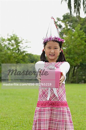 Girl with party hat holding pink gift box towards camera