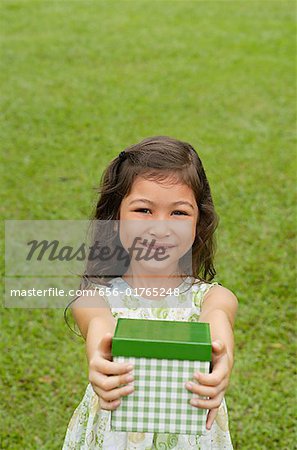 Girl standing on grass, holding gift box towards camera