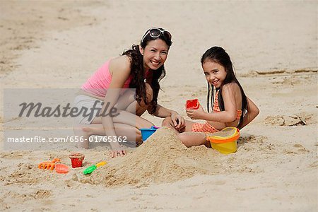 Mother and daughter on beach, building sand castle