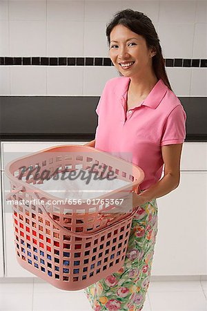 Woman doing laundry, holding laundry basket, smiling looking at camera