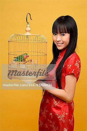 Young woman holding lovebird in bird cage, smiling