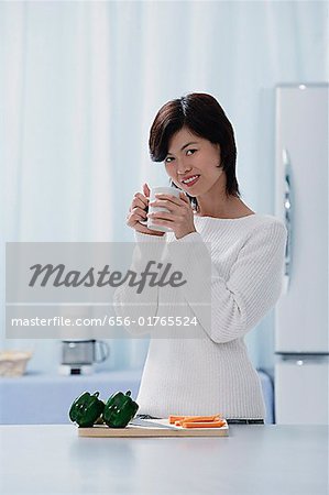 Woman in kitchen, holding a mug, looking at camera