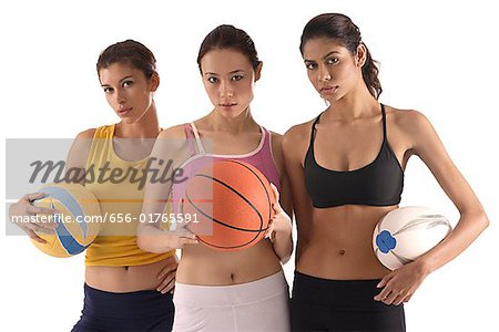 three women of different race, holding volleyball, basketball, and rugby ball, looking at camera