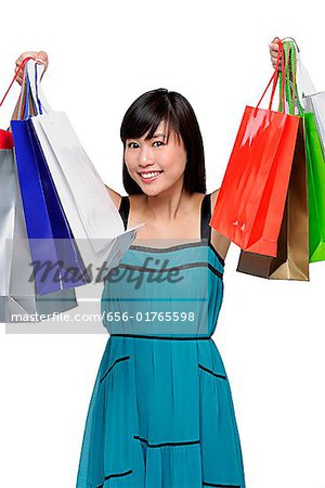 Young woman wearing blue dress and holding shopping bags up in air