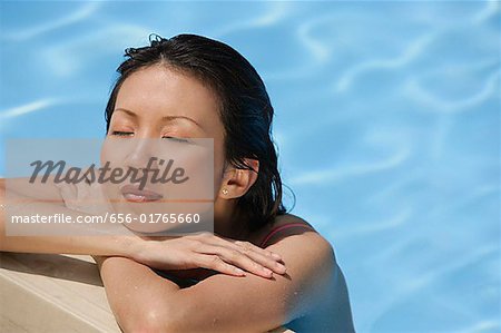 Woman leaning at the edge of swimming pool, arms crossed, eyes closed