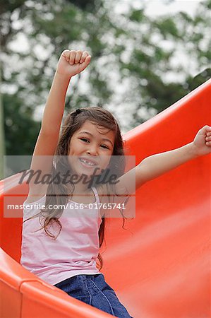 Girl coming down playground slide arms outstretched