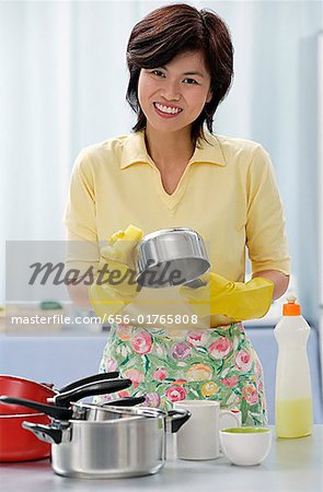 Woman in kitchen, cleaning pots and pans, smiling at camera