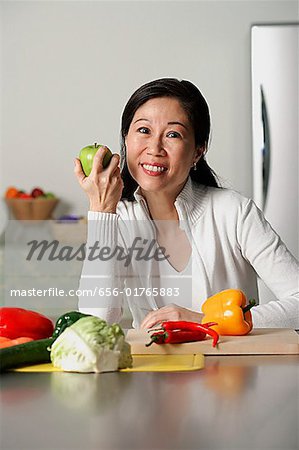 Femme dans la cuisine, tenant une pomme, légumes sur une table autour d'elle