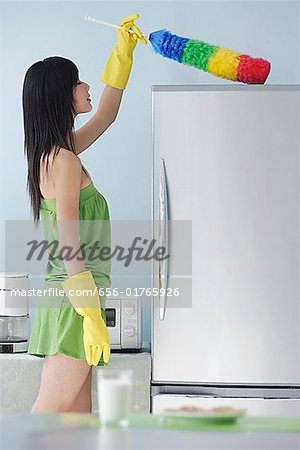 woman in kitchen, dusting, cleaning, top of fridge