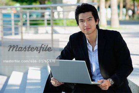 A man uses his laptop outdoors while he looks at the camera