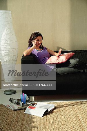A teenage girl sits on the couch and talks on the phone