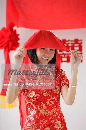 A bride wearing a red silk dress smiles at the camera