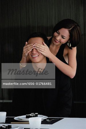A woman covers her boyfriends eyes as she prepares to surprise him with dinner
