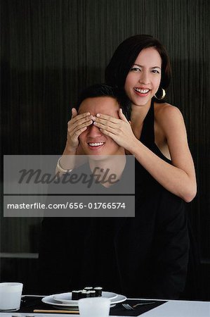 A woman covers her boyfriends eyes as she prepares to surprise him with dinner