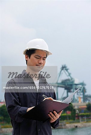 Man with hard helmet writing on clipboard