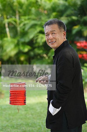 Man in traditional clothing, standing in park holding Chinese lantern