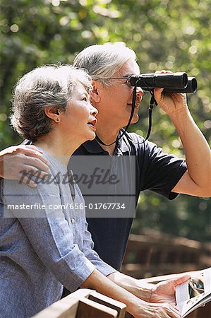 Senior couple side by side, man using binoculars