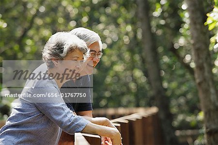 Mature couple leaning on railing, smiling, looking away