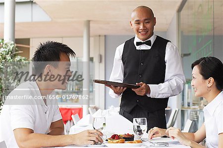 Couple in restaurant, waiter standing next to their table