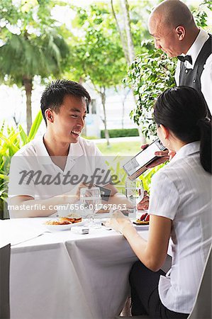 Couple in restaurant, waiter standing next to their table with bill