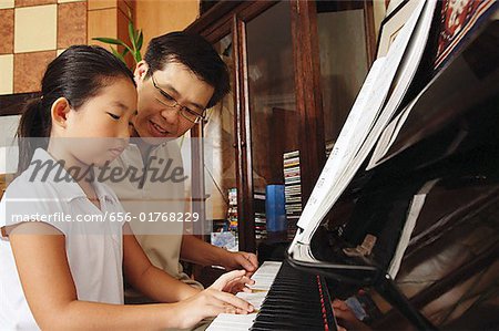 Fille de jouer du piano, père assis à côté d'elle