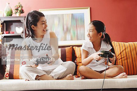 Mother and daughter on sofa, holding video game controllers, looking at each other