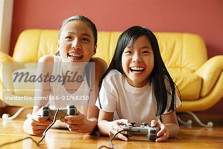 Zwei Schwestern im Wohnzimmer, liegend auf dem Boden spielen von Videospielen