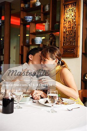 Couple in Chinese restaurant, toasting with wine glasses, man kissing woman on cheek