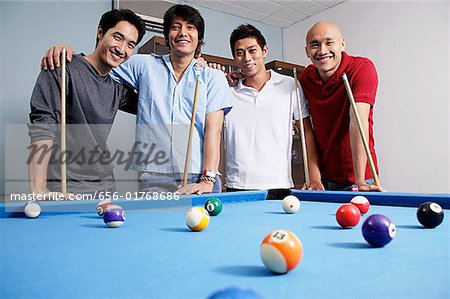 Männer stehen um Pool-Tisch, Blick in die Kamera