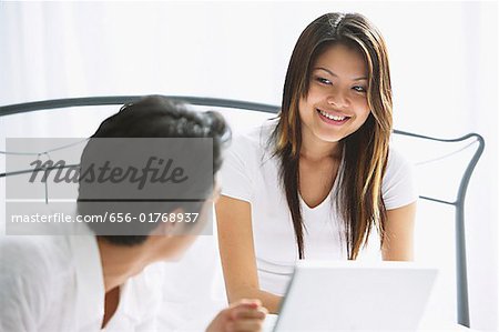Couple dans la chambre à coucher, femme, sourire aux lèvres, l'homme regardait, ordinateur portable devant elle