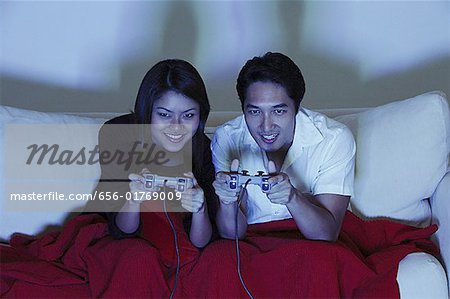 Couple sitting side by side on sofa, playing with video games