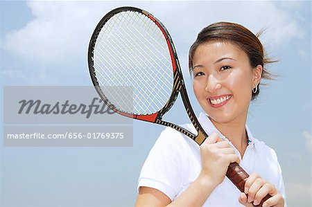 Jeune femme tenant une raquette de tennis souriant à la caméra