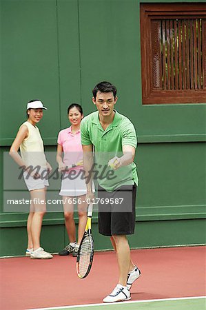 Man serving a game of tennis with two women watching