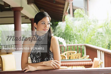 Woman wearing halter top, leaning on railing, arms crossed