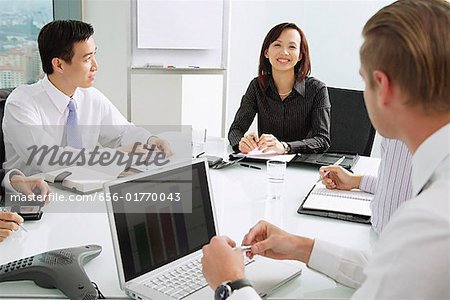 Businesswoman at head of table, smiling, male executives sitting around her