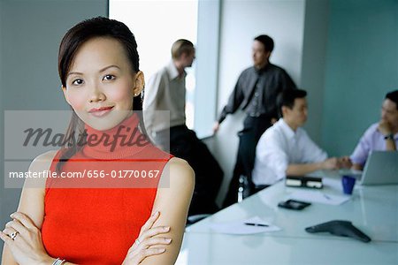 Female executive, arms crossed, looking at camera, people in the background