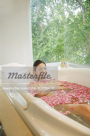 Woman lying in bath tub, flowers floating in water