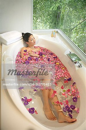 Woman in bathtub, flowers floating in water
