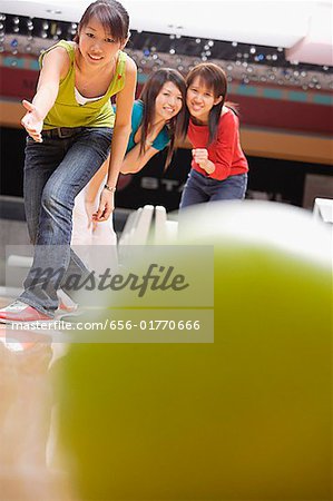 Young woman bowling, friends watching behind her