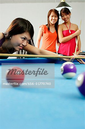 Woman holding pool cue, aiming, women watching in the background