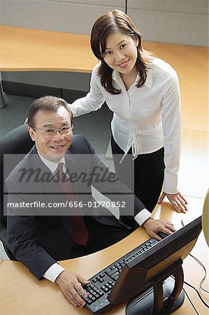 Businessman and woman in office cubicle, looking up at camera