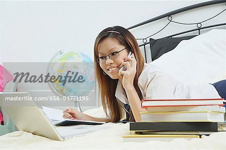 Girl lying on bed, using laptop and mobile phone