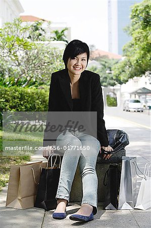 Femme assise dans la ville, sacs à provisions autour d'elle, souriant à la caméra