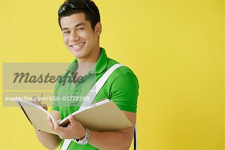 Young man writing in notebook, looking at camera