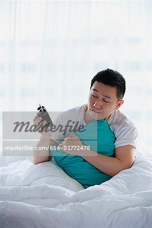 Man sitting in bed, holding alarm clock