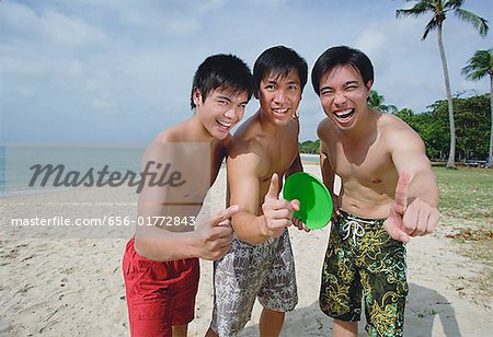 Men on beach, standing side by side, making hand sign